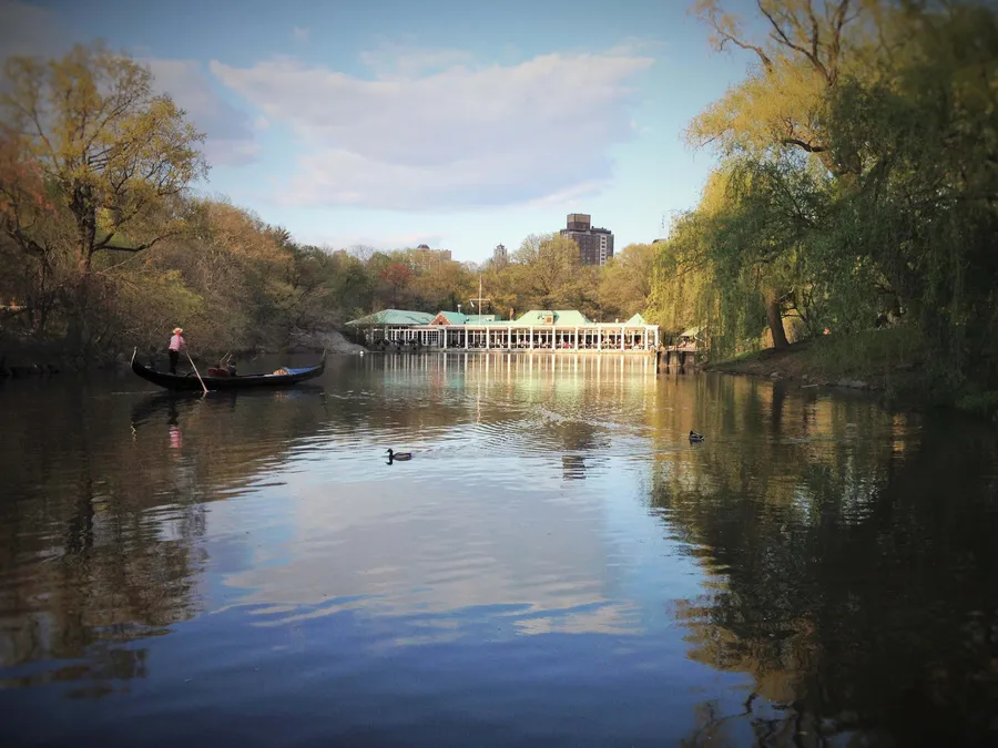 A gondola on the lake in Central Park, New York, with the boathouse reflected in still water, photograph by Esther Piaskowski